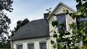 A two-story house with a sloped roof, a front porch, and a well-maintained garden with various plants and flowers. - Ferienwohnung an der Ostsee (Hasselberg)