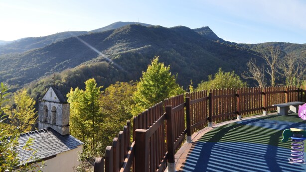 Vista panorámica de un paisaje montañoso con una cerca de madera y un pequeño edificio con un campanario.