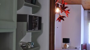 Una habitación con techo de madera, un escritorio con lámpara y una silla. Se ven estantes con varios objetos.