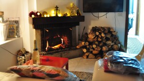Una sala de estar acogedora con chimenea, televisor montado en la pared y una pila de leña.