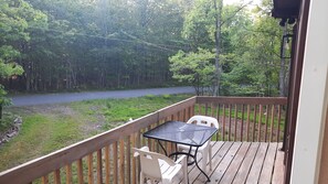 Une terrasse en bois avec une table et des chaises, donnant sur une route et une zone boisée.