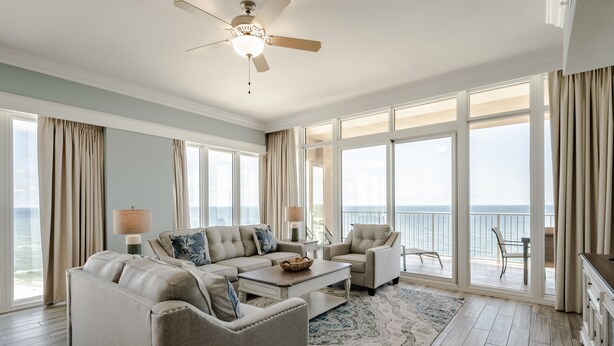 A spacious living room with a large sofa, a coffee table, and a view of the ocean through large windows. - Luxury Direct Beachfront Corner Unit Lazy River-Waterslide-Walk to Restaurant's (Orange Beach)
