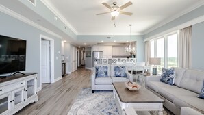 A spacious living room with a television, sofa, coffee table, and a ceiling fan. - Luxury Direct Beachfront Corner Unit Lazy River-Waterslide-Walk to Restaurant's (Orange Beach)