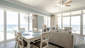 A spacious room with a dining table, chairs, a sofa, and a ceiling fan. Large windows offer a view of the ocean. - Luxury Direct Beachfront Corner Unit Lazy River-Waterslide-Walk to Restaurant's (Orange Beach)