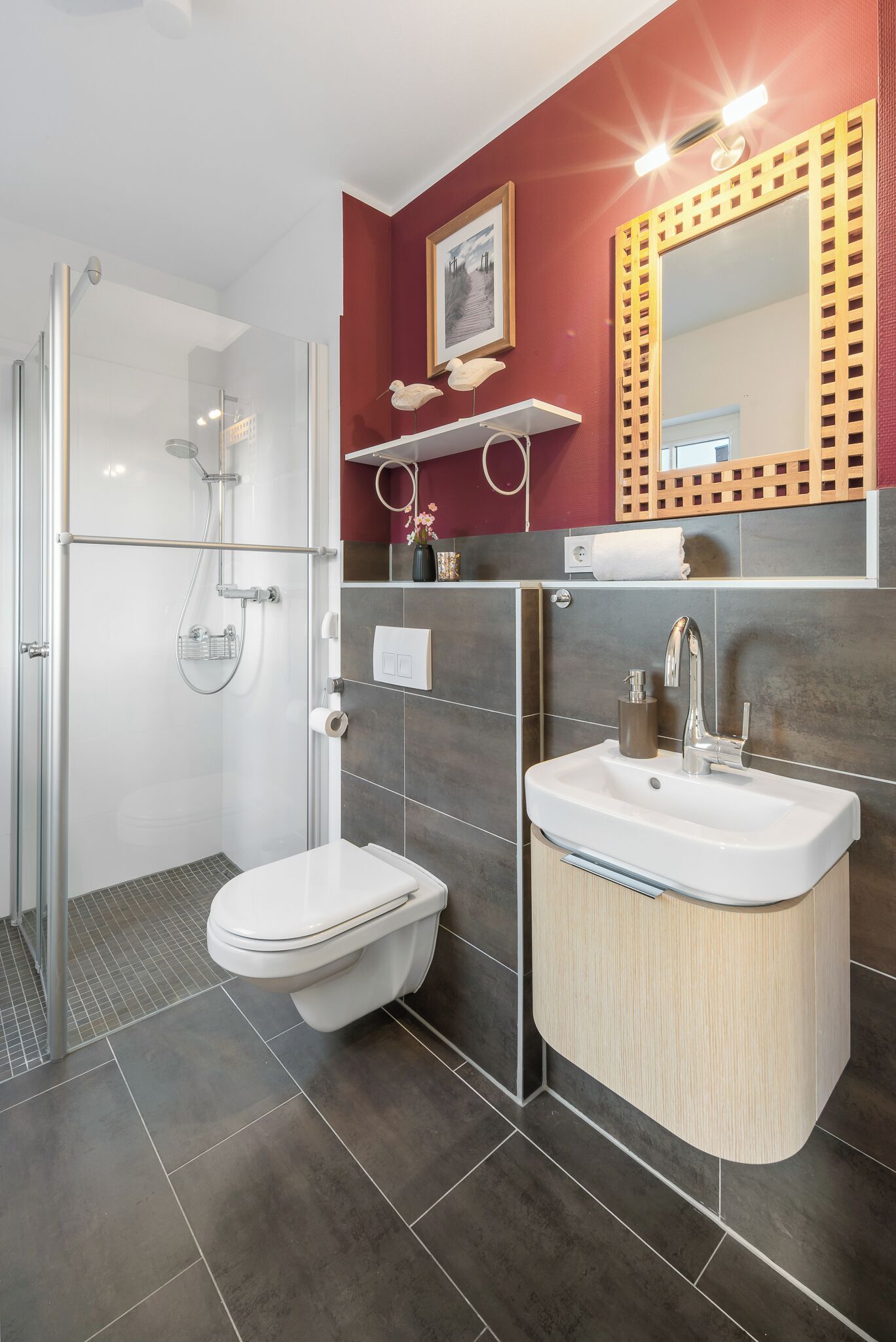 Une salle de bain moderne dotée d’une douche à parois de verre, de toilettes blanches, d’un lavabo avec un meuble-vasque en bois et d’un miroir orné d’un cadre décoratif.