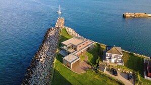 A coastal property with a stone pier, a grassy lawn, and a building with a sloped roof. - Land`s End - Blick auf die Freie Ostsee, Sauna, Wintergarten, Elektro Grill (Olpenitz)