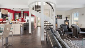 A modern interior with a central spiral staircase, a kitchen with red accents, and a seating area with leather sofas. - Land`s End - Blick auf die Freie Ostsee, Sauna, Wintergarten, Elektro Grill (Olpenitz)