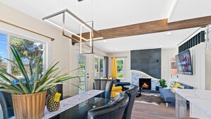 A modern living room with a fireplace, a dining area with a glass table, and a seating area with sofas and chairs.
