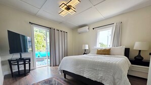 A bedroom with a large bed, a TV, a nightstand, and a window with curtains.