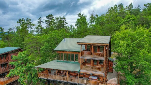A multi-story log cabin with a balcony and a deck, surrounded by dense forest. - "Shine Valley #53" View for days (sevierville)