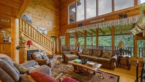 A spacious wooden cabin with a high ceiling, a staircase leading to an upper level, and a cozy living area with a sofa, armchairs, and a coffee table. - "Shine Valley #53" View for days (sevierville)