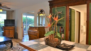 A living room with a checkered floor, a wooden cabinet, a television, a dining table, and a decorative plant centerpiece. - Gorgeous*Peaceful*Condo* Steps to beautiful beach (Kihei)