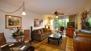 A living room with a sofa, coffee table, and chairs, a television, and a balcony with a view. - Gorgeous*Peaceful*Condo* Steps to beautiful beach (Kihei)