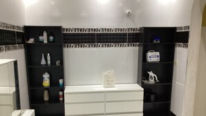 Une salle de bain avec un meuble-lavabo blanc, des étagères noires où sont rangés les articles de toilette et un porte-serviettes blanc.
