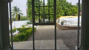 Une vue à travers une fenêtre donnant sur une cour arrière avec une terrasse, une piscine et une clôture blanche.