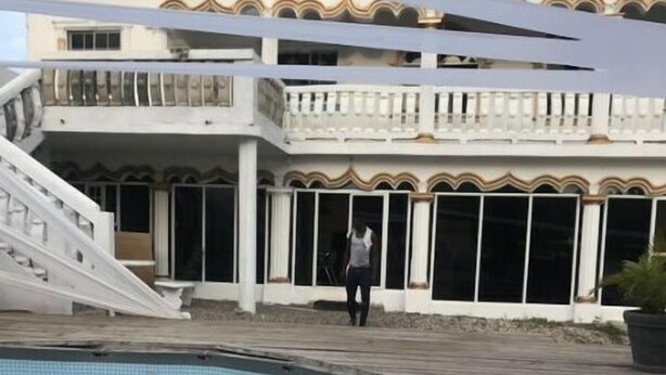 Une piscine avec une terrasse en bois, un escalier menant à un balcon et un bâtiment doté de grandes fenêtres et de moulures décoratives.