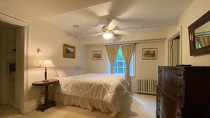 A bedroom with a bed, a dresser, a ceiling fan, and a window with curtains. - Enderly - c1859 - English Basement Apartment (Charlottesville)