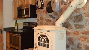 A rustic kitchen with a stone wall, wooden cabinets, a white stove, and hanging pots. - Enderly - c1859 - English Basement Apartment (Charlottesville)