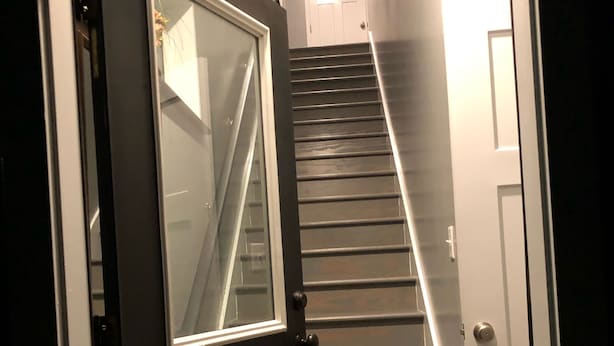 A staircase with a dark door at the bottom and a light fixture above it. - Newly Constructed Second Floor Modern Studio Apartment Unit 2 ~ Sleeps 6 (Accomac)