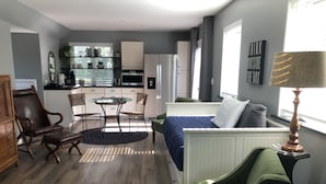 A compact hotel room with a bed, a small dining table with chairs, a kitchenette, a window with curtains, and a lamp. - Newly Constructed Second Floor Modern Studio Apartment Unit 2 ~ Sleeps 6 (Accomac)