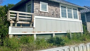 A two-story house with a metal roof, a large window, and a wooden deck. - Charming Studio / Cottage in Marina BHI & Shoals Club Available (Bald Head Island)