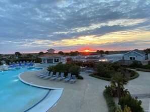 Zona de piscina en un resort con sillones de descanso, un pabellón y vistas al atardecer.