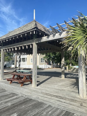 A wooden gazebo with a tiled roof, a picnic table, and a white picket fence in the background.