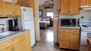 A compact kitchen with wooden cabinets, a coffee maker, a microwave, and a stove. A bedroom is visible through an open doorway. - Tranquil Desert Retreat (Tucson)