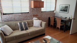A living room with a beige sofa, a glass coffee table, a brick wall, and a dining area with a small table and chairs. - Tranquil Desert Retreat (Tucson)