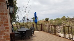 A wooden deck with a table and chairs, a blue umbrella, and a view of a desert landscape. - Tranquil Desert Retreat (Tucson)