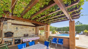 Une terrasse extérieure avec une cheminée en pierre, une piscine et des chaises bleues.