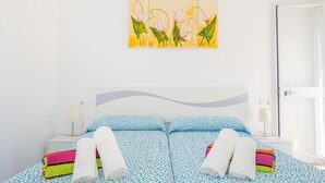 Ein ordentlich gemachtes Bett mit einer blau-weißen Bettdecke, zwei aufgerollten weißen Handtüchern und bunten Handtüchern daneben.