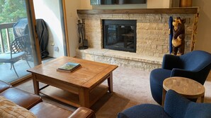 Ein gemütliches Wohnzimmer mit Kamin aus Stein, Couchtisch aus Holz, Ledersitzmöbel und einem blauen Sessel.
