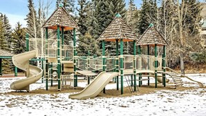 Ein Spielplatz mit einer Wendelrutsche, einer geraden Rutsche und einer Kletterkonstruktion, umgeben von Bäumen.