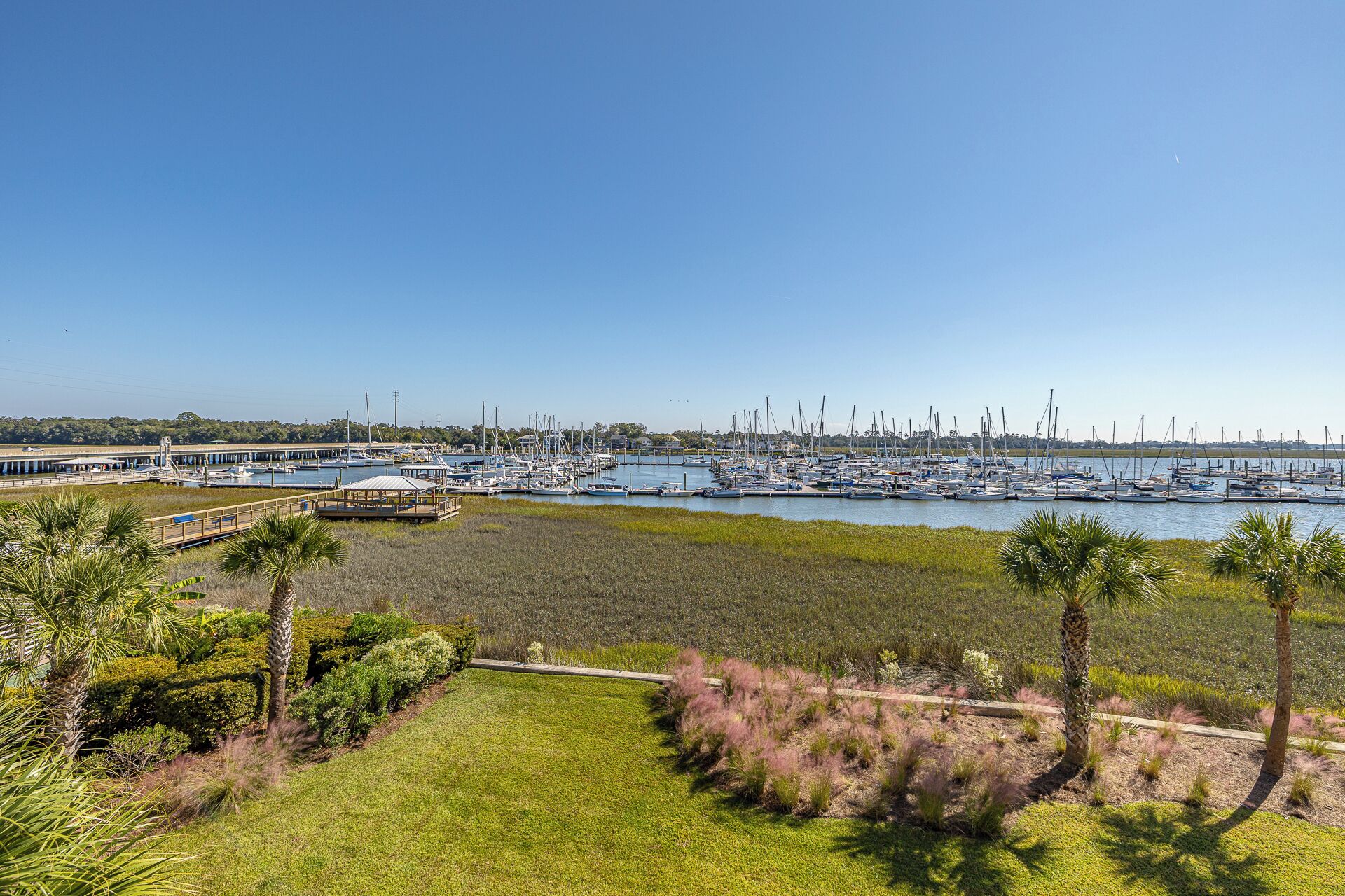 A marina with numerous boats docked, surrounded by grassy areas and palm trees.
