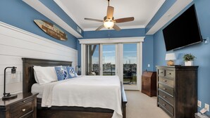 Une chambre à coucher comprenant un lit, une table de chevet, une commode, un téléviseur et un ventilateur de plafond.