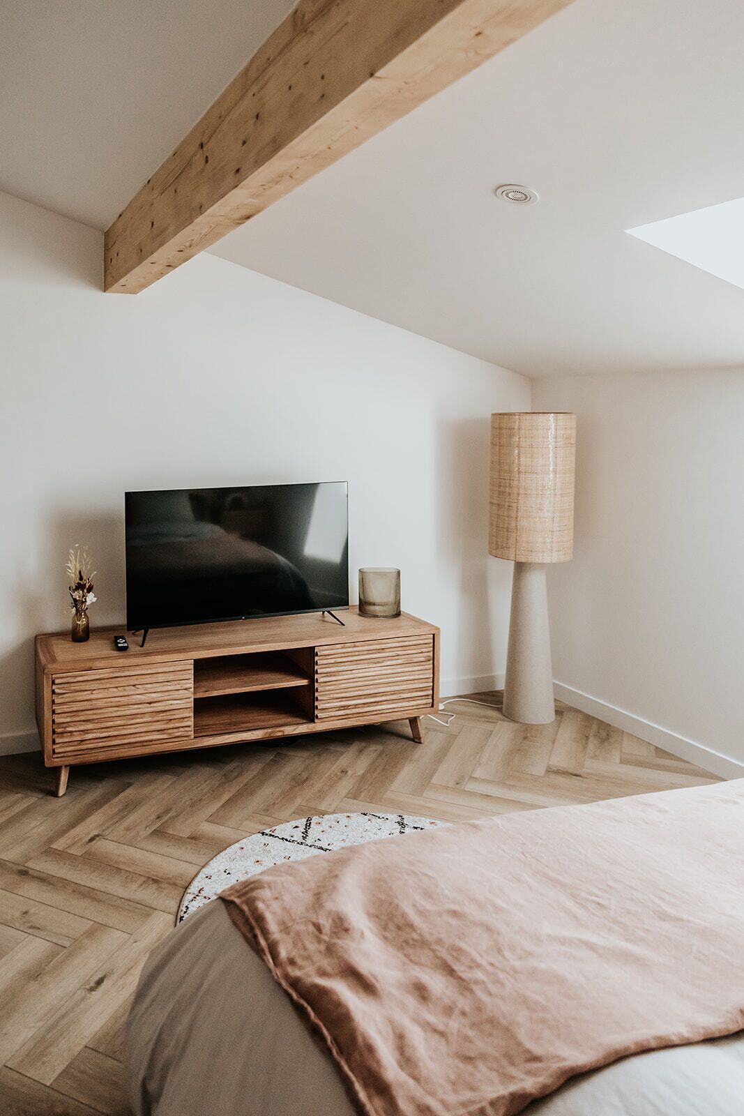 Ein modernes Schlafzimmer mit einer Holztv-Konsole, einem großen Fernseher, einer Stehlampe und einem Bett mit rosa Decke.