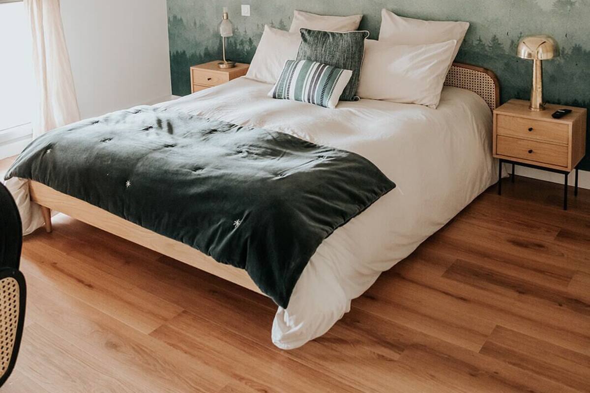 A bedroom with a wooden bed, a nightstand with a lamp, and a wall mural.