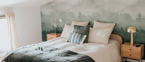 A bedroom with a wooden bed, a nightstand with a lamp, and a wall mural.