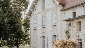 A large stone building with a red-tiled roof, multiple windows, and a well-maintained garden with various plants and flowers. - Château La Grande Clotte (Lussac)