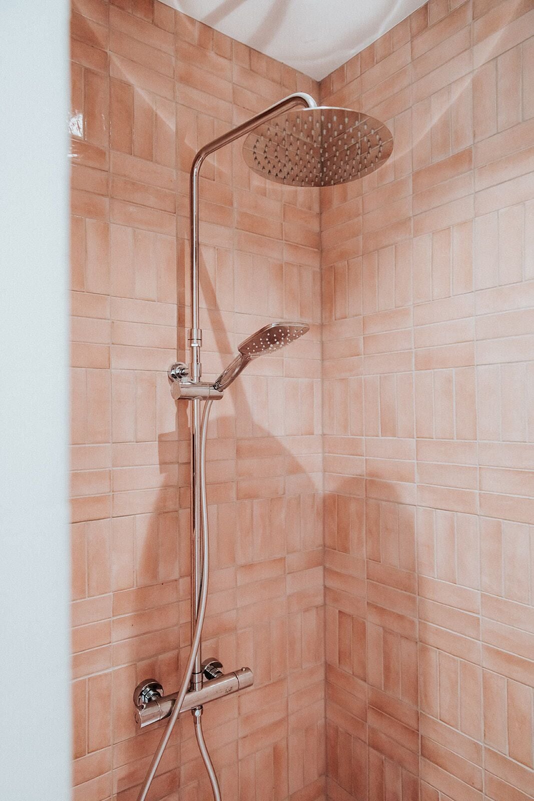 Una ducha con cabezal de ducha manual y otro cabezal de lluvia montado en la pared, frente a un muro de azulejos.