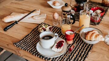 Un desayuno con pan, croissants, una taza de café, un vaso de zumo de naranja y un bol pequeño de fruta.