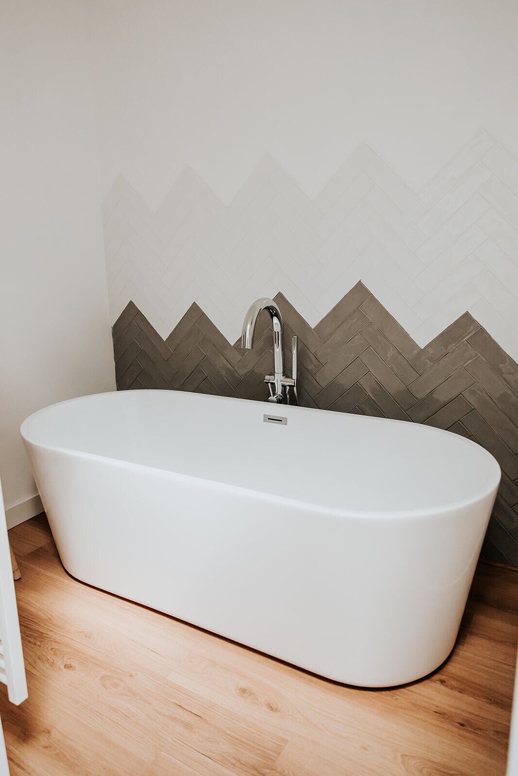 Un baño moderno con una bañera independiente, un grifo cromado y un revestimiento de pared con motivo de espiga.