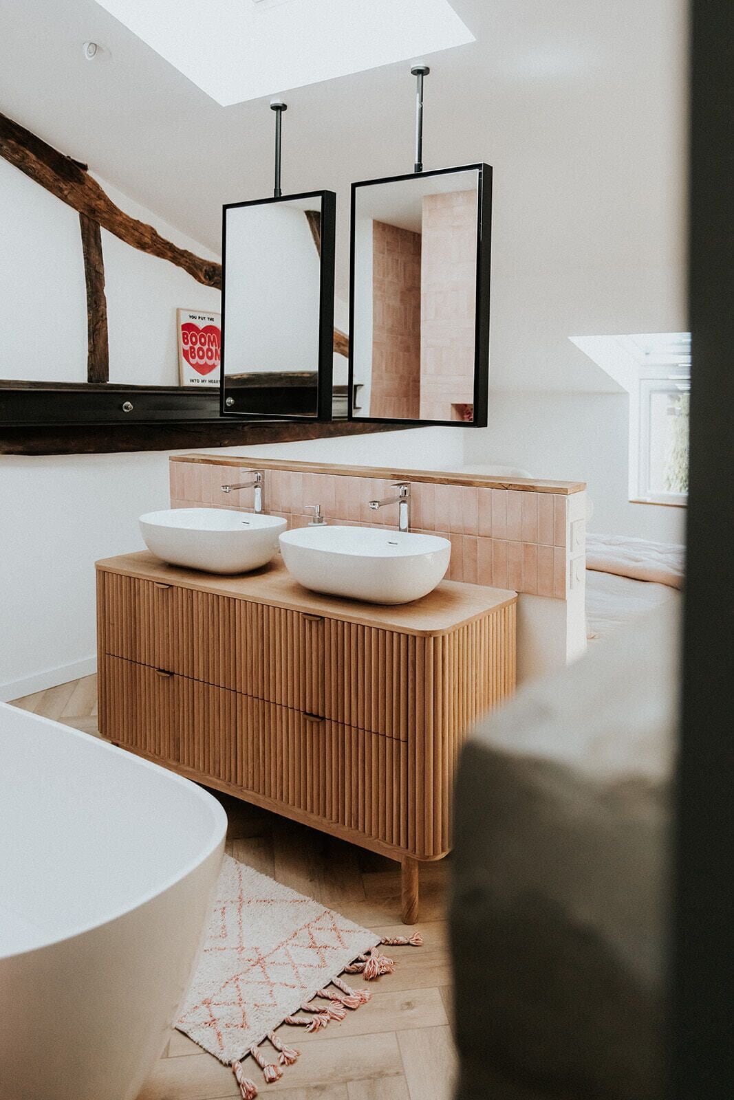 A modern bathroom with a wooden vanity, two white sinks, a large bathtub, and a skylight.
