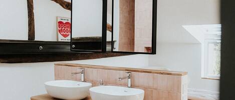 Un baño moderno con tocador de madera, dos lavamanos blancos, una bañera grande y un tragaluz.