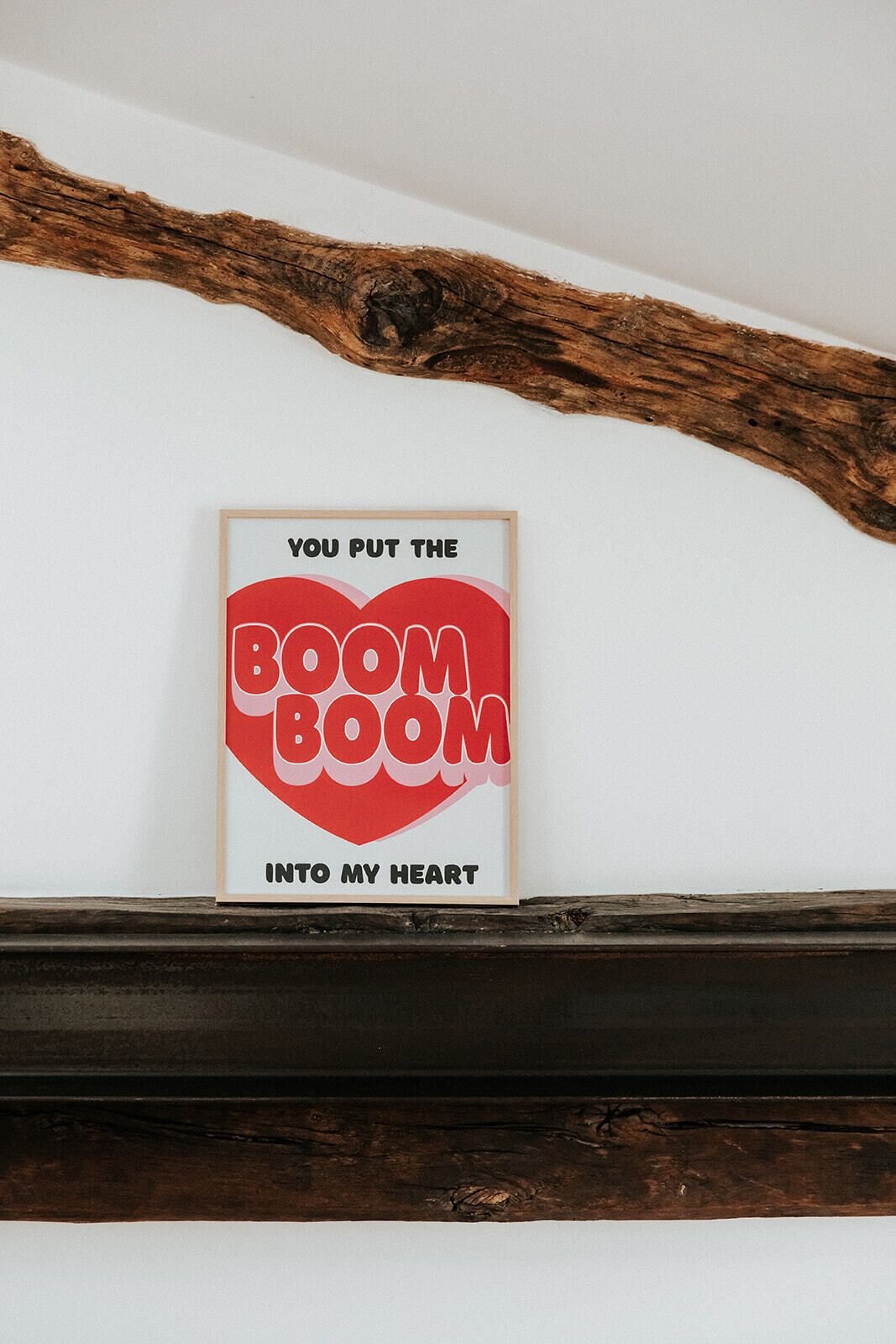 Een lijst met de tekst 'YOU PUT THE BOOM INTO MY HEART' aan een witte muur boven een donker houten schoorsteenmantel.
