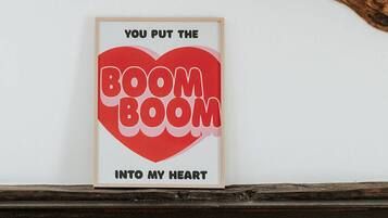 Een lijst met de tekst 'YOU PUT THE BOOM INTO MY HEART' aan een witte muur boven een donker houten schoorsteenmantel.