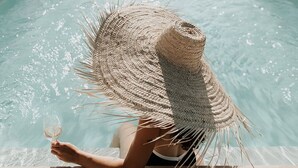 A person relaxing by a pool with a straw hat, holding a glass of wine. - Château La Grande Clotte (Lussac)