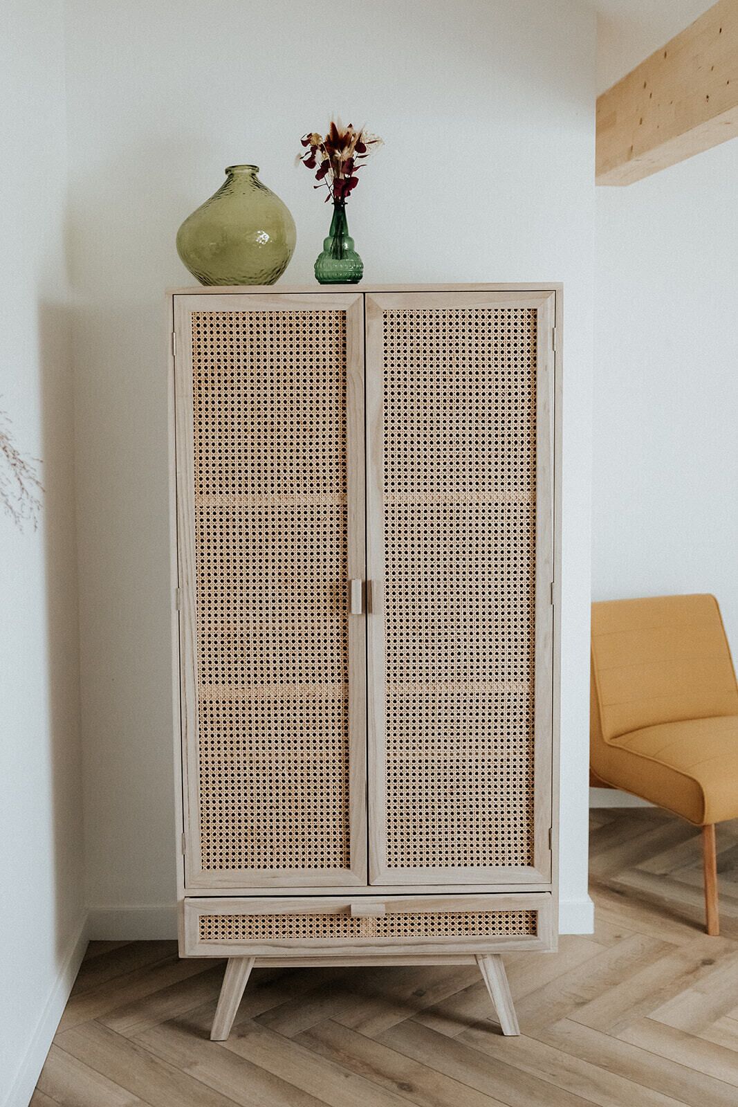 Um guarda-roupa de vime com duas portas, um vaso verde e uma cadeira amarela.