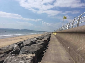 A coastal walkway with a concrete barrier, a sandy beach, and the ocean in the background.